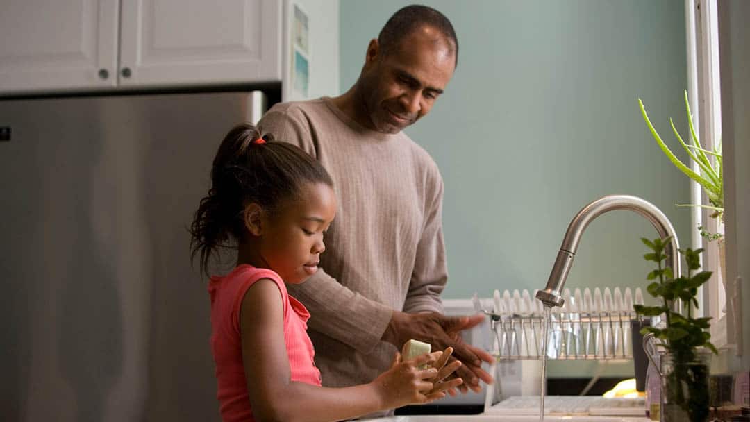 Dad teaching daughter to wash hands by kitchen sink