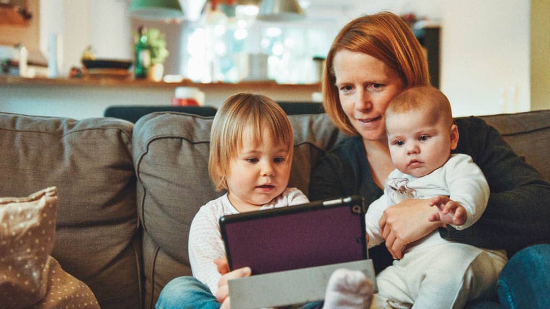 Middle-aged mom sitting with her two kids watching a tablet